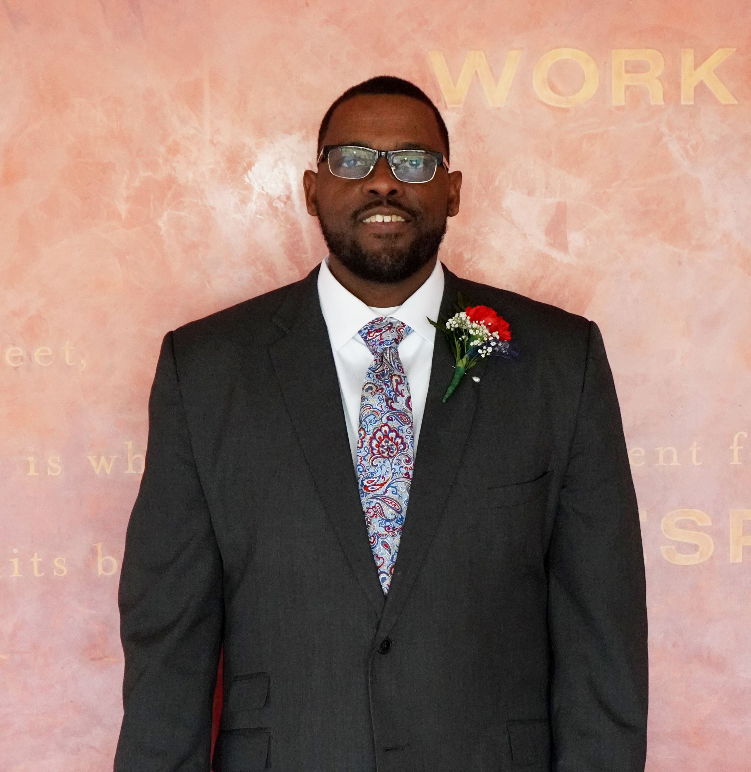 Tall african american man with glasses and short hair smiling in a black suite