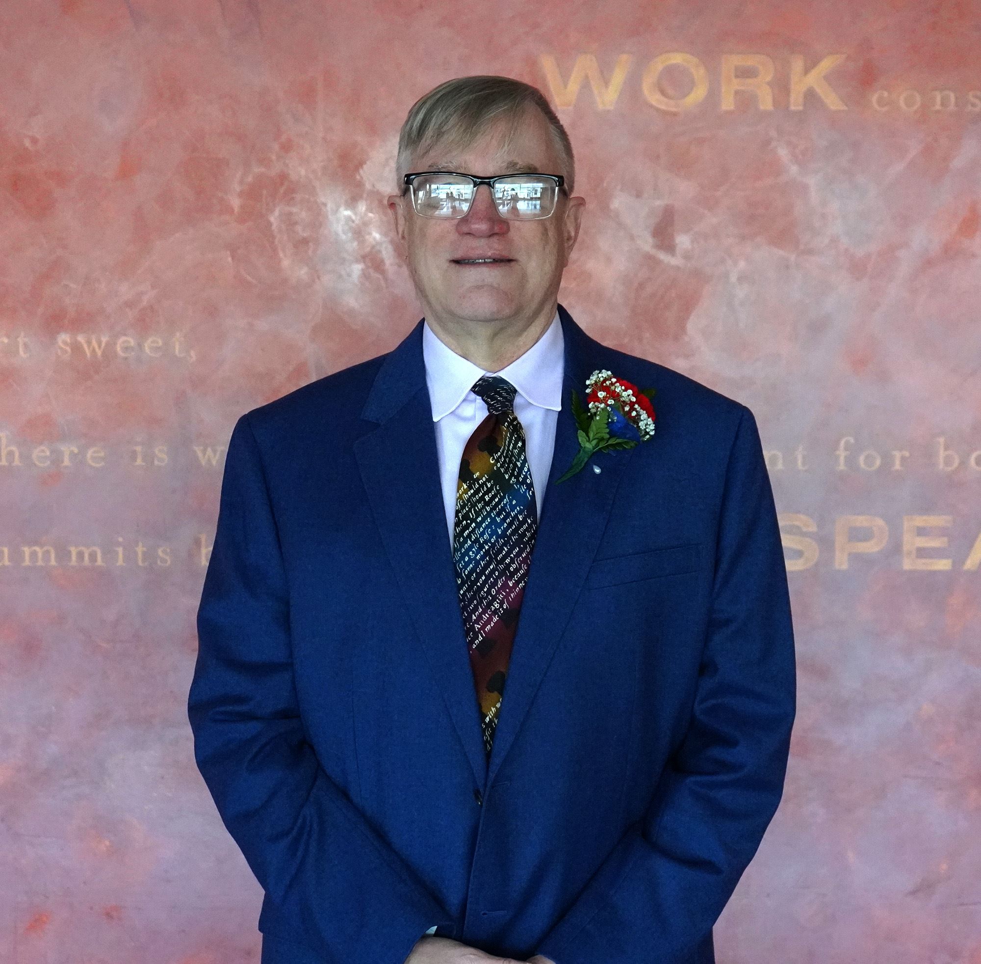 Tall white male with glasses wearing a blue suite smiling 