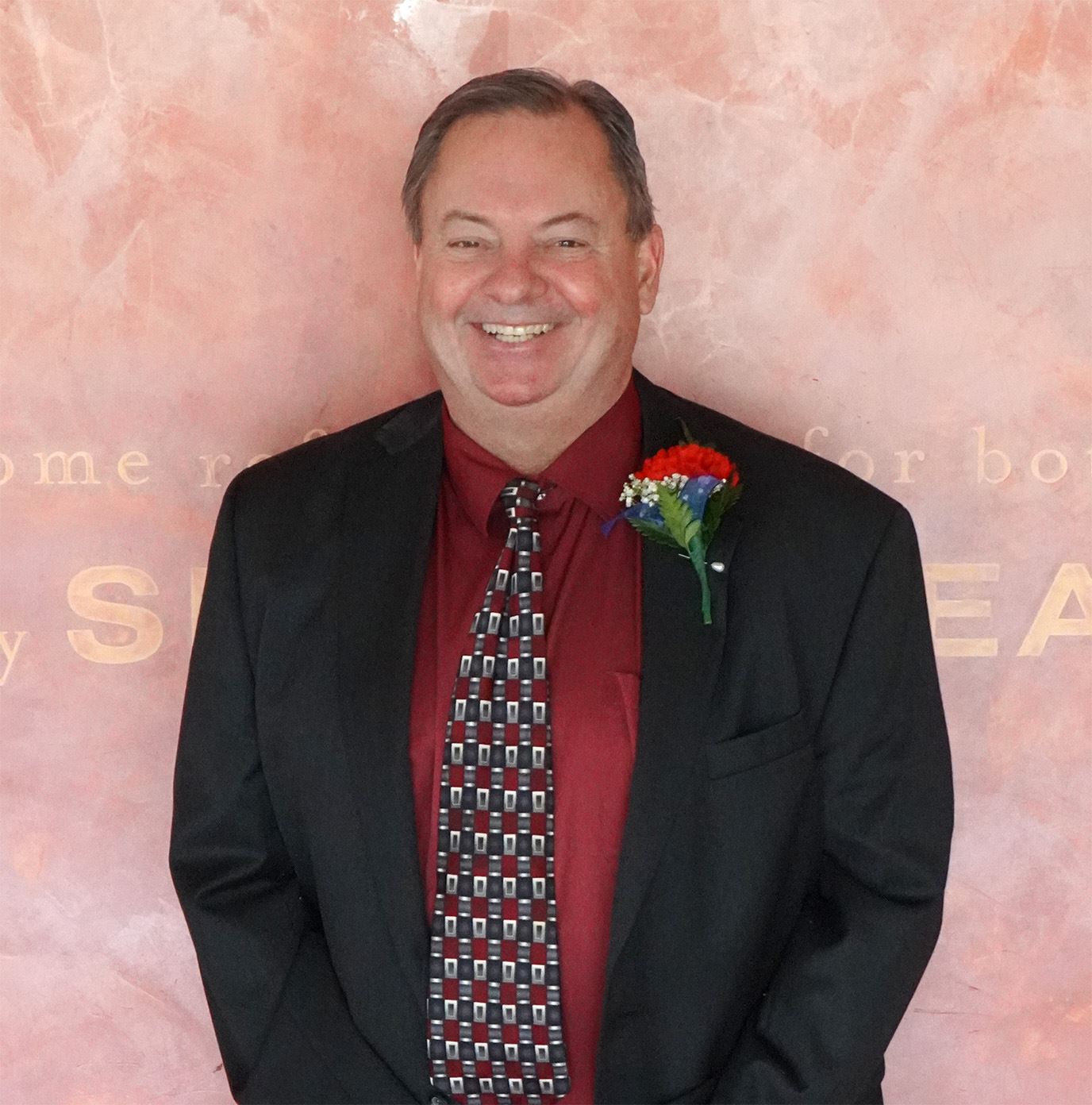 Shorter white male with black suite red shirt smiling